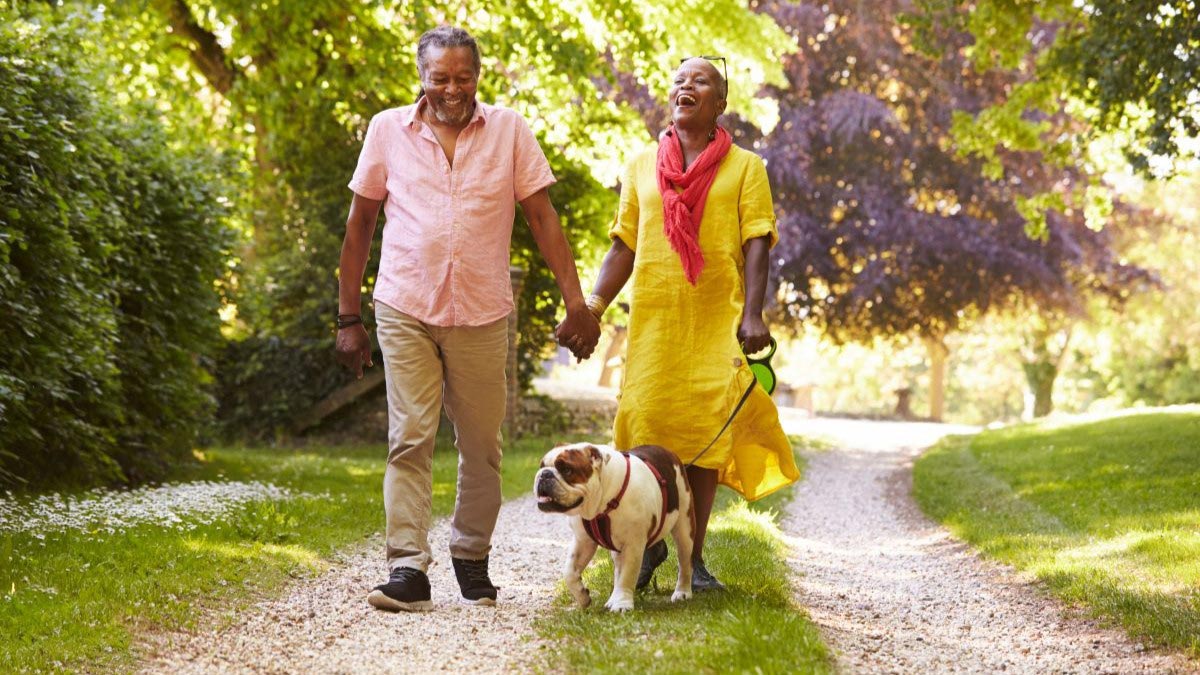 Senior Couple Walking With Pet Bulldog In Countryside