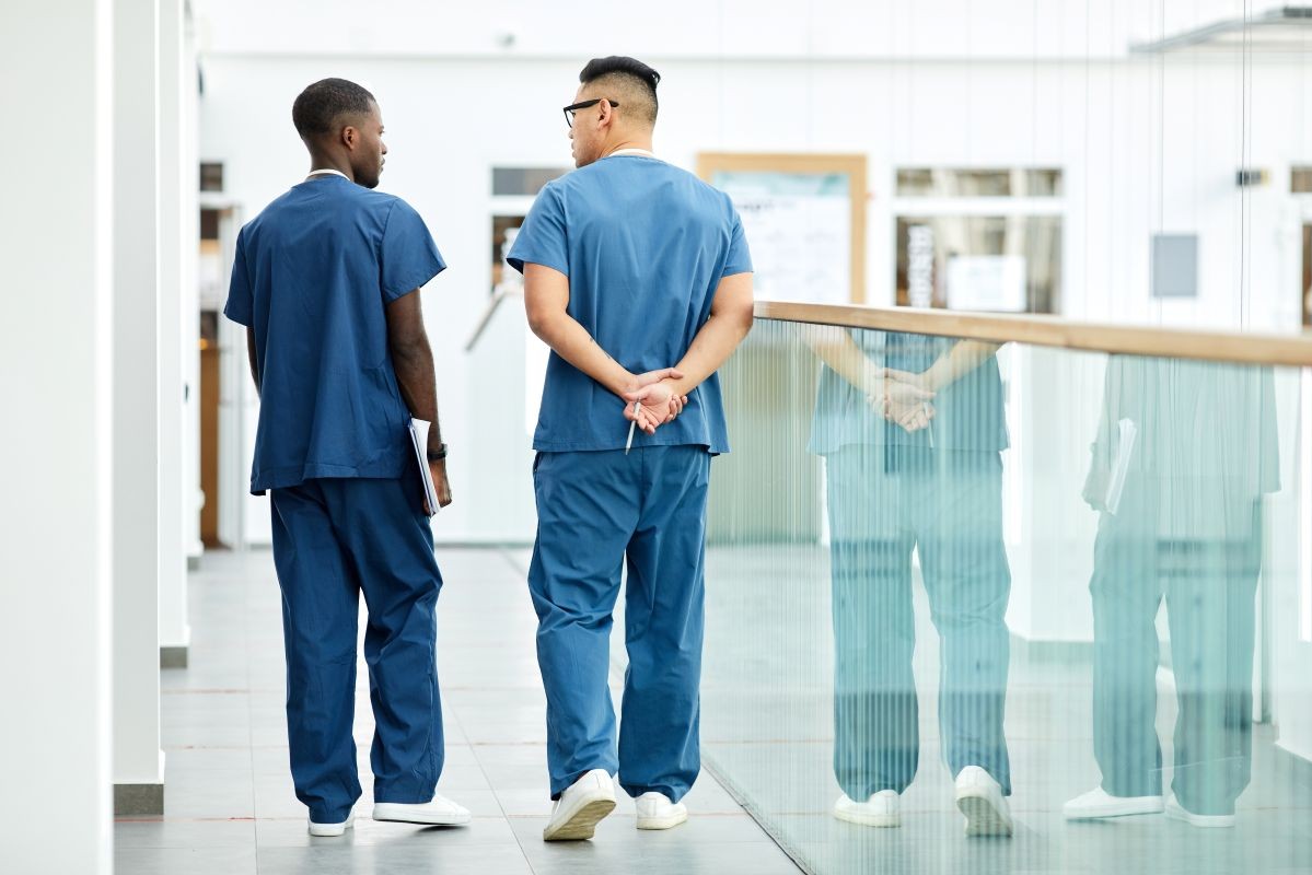back of two healthcare workers walking down hospital hallway