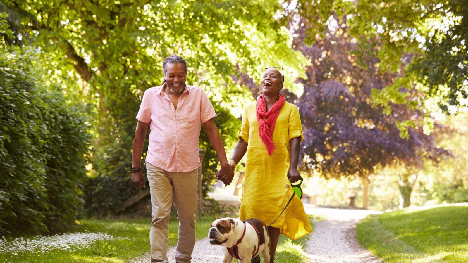 Senior Couple Walking With Pet Bulldog In Countryside