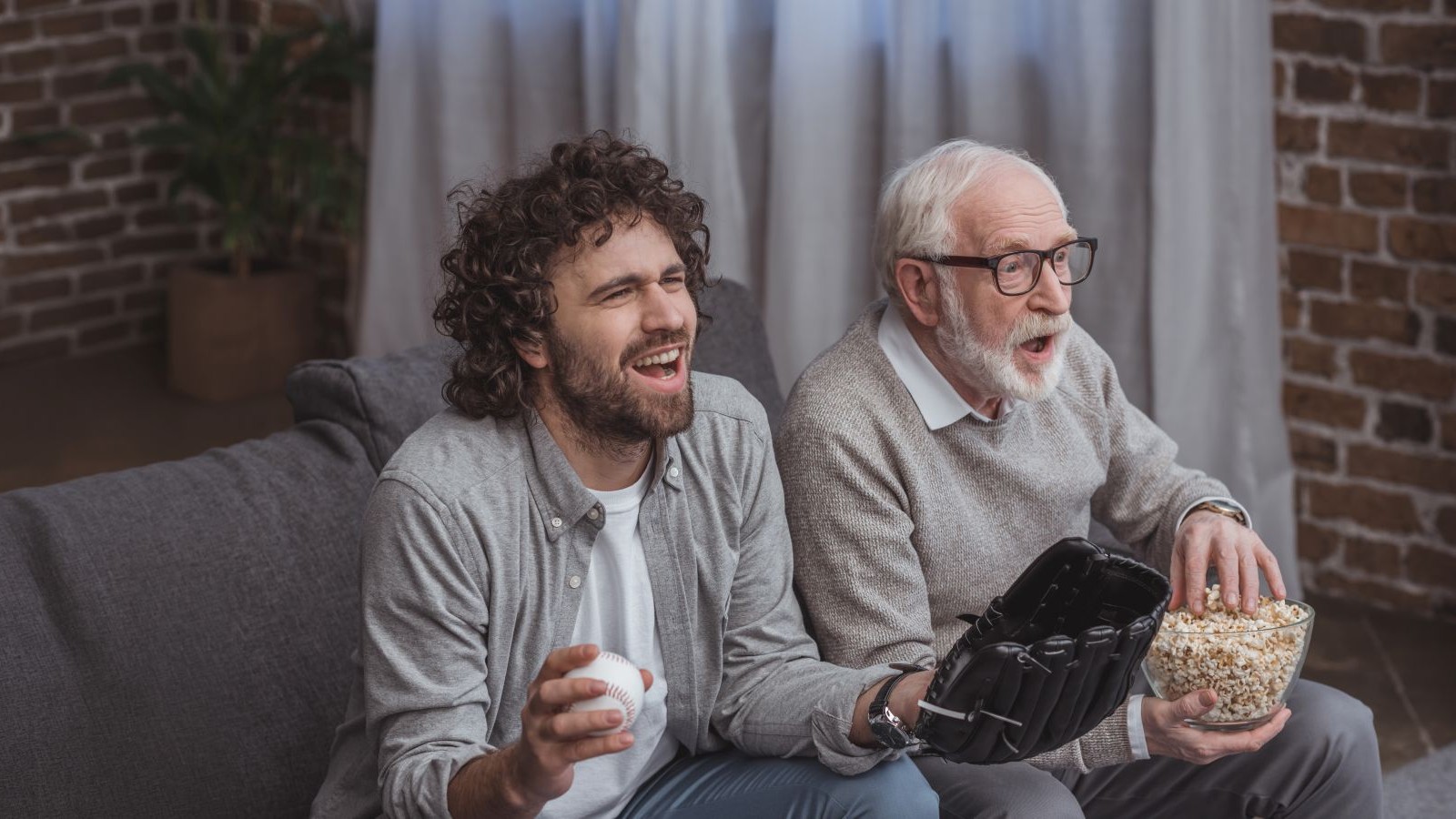 adult son and senior father cheering on baseball team and watching game at home